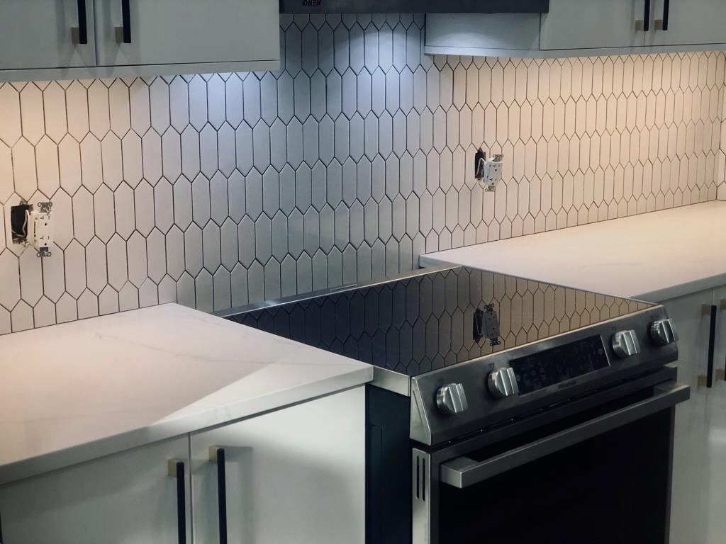 Black glass cooktop and stainless range set into a white picket tile backsplash with dark grout and two-tone cabinet handles
